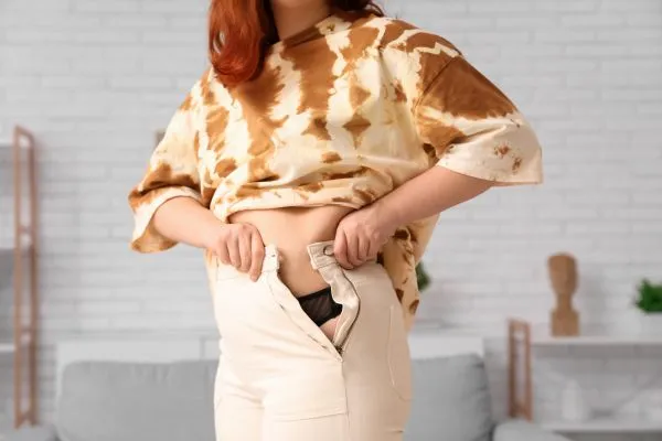 Image of woman trying to do her trousers up after pregnancy weight gain Leighton Buzzard